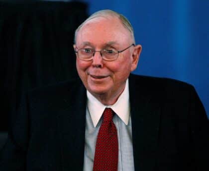 Charlie Munger szemüvegben vörös nyakkendővel fehér ingben sötét zakóban mosolyog