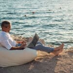 férfi laptop tengerpart babzsákon ül az ember